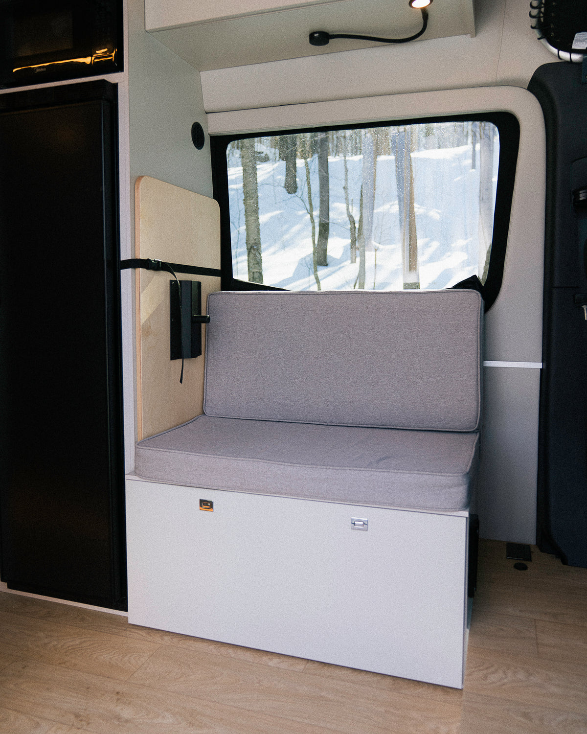 Banc convertible avec coussin et dossier en espace garage van New West, vue vers fenêtre sur forêt enneigée