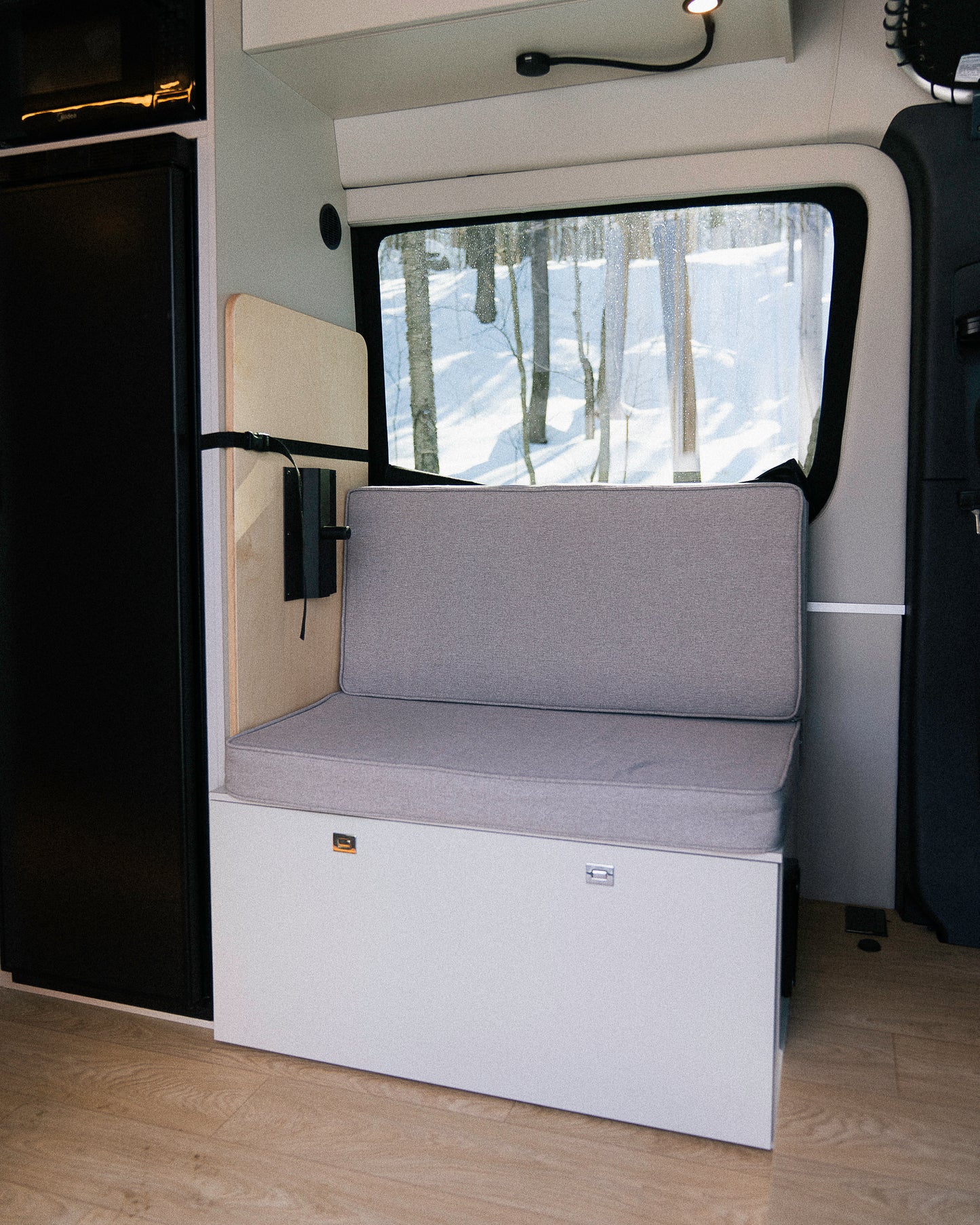 Banc convertible avec coussin et dossier en espace garage van New West, vue vers fenêtre sur forêt enneigée