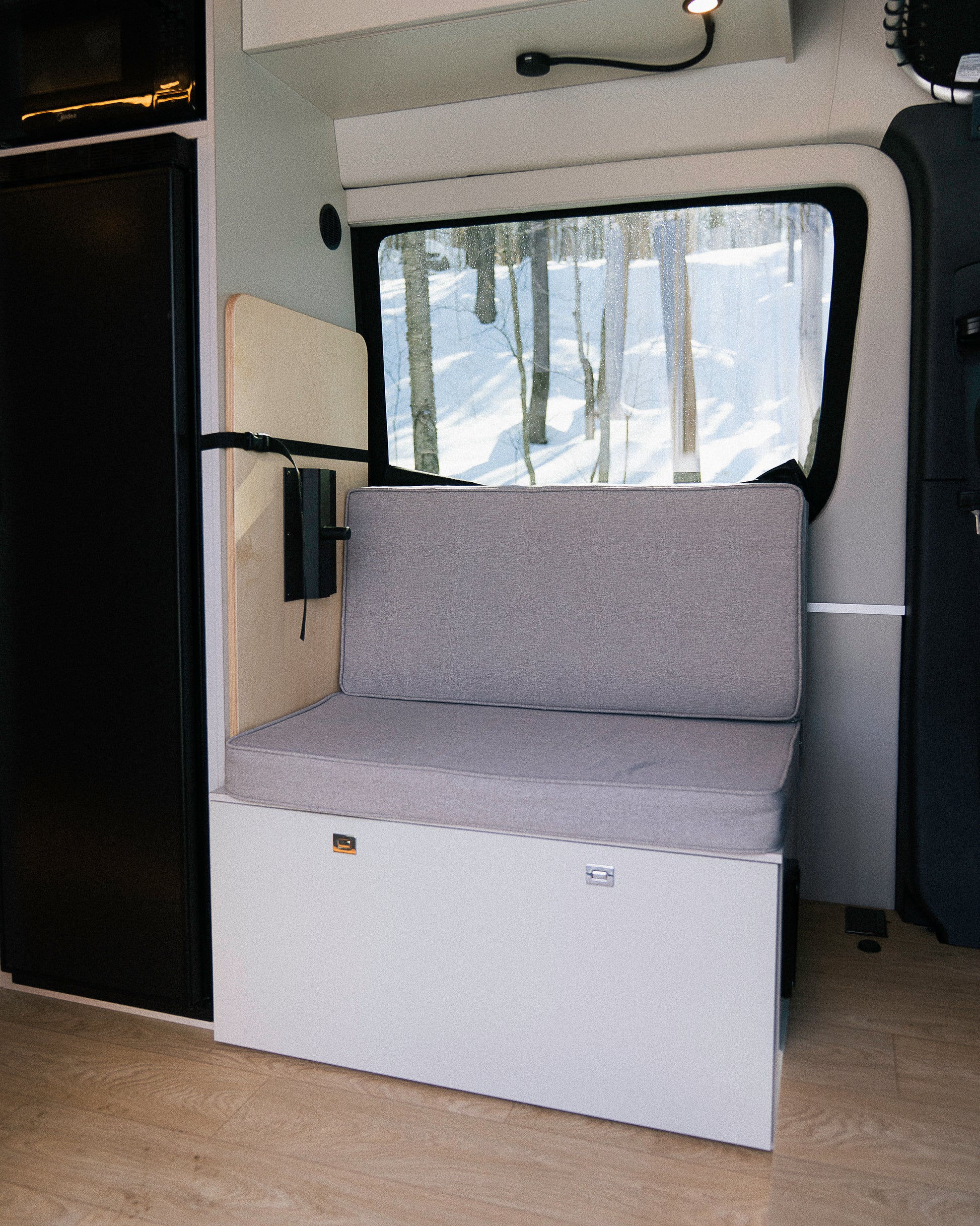 Banc convertible avec coussin et dossier en espace garage van New West, vue vers fenêtre sur forêt enneigée